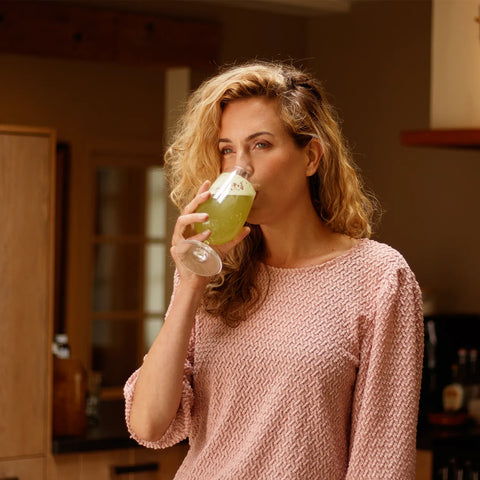 Eine Frau trinkt genussvoll ihr SuperGreens-Getränk von NutraLinea – mit grünen Superfoods, Vitaminen und Mineralstoffen für natürliche Energie und nur 11 kcal pro Portion.