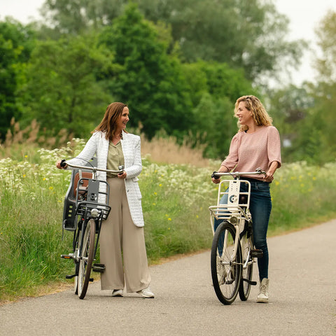 Zwei Frauen stehen mit ihren Fahrrädern inmitten grüner Natur und lachen sich an – ein Moment voller Lebensfreude, Balance und aktiver Weiblichkeit, ganz im Sinne des NutraLinea-Lifestyles.