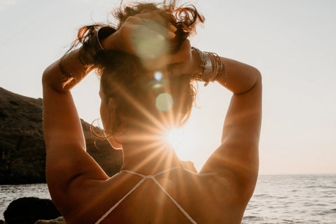 Frau sitzt am Strand und beobachtet den Sonnenuntergang